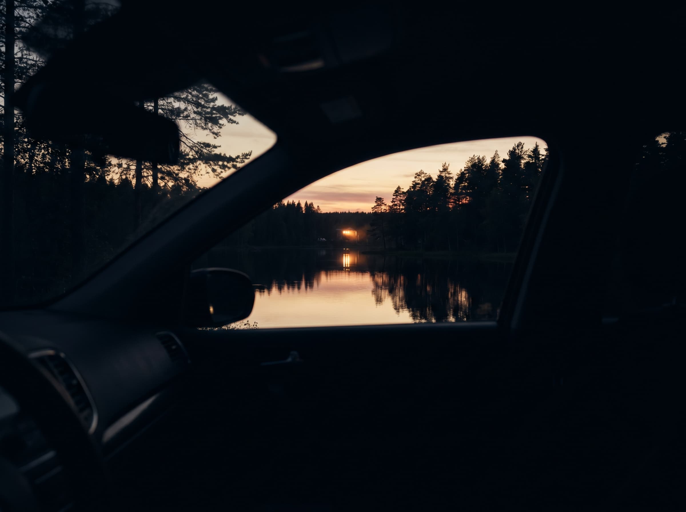 Vue à travers la vitre d'un véhicule sur le lac du Malsaucy au crépuscule, point lumineux du festival éclairé sur la rive opposée